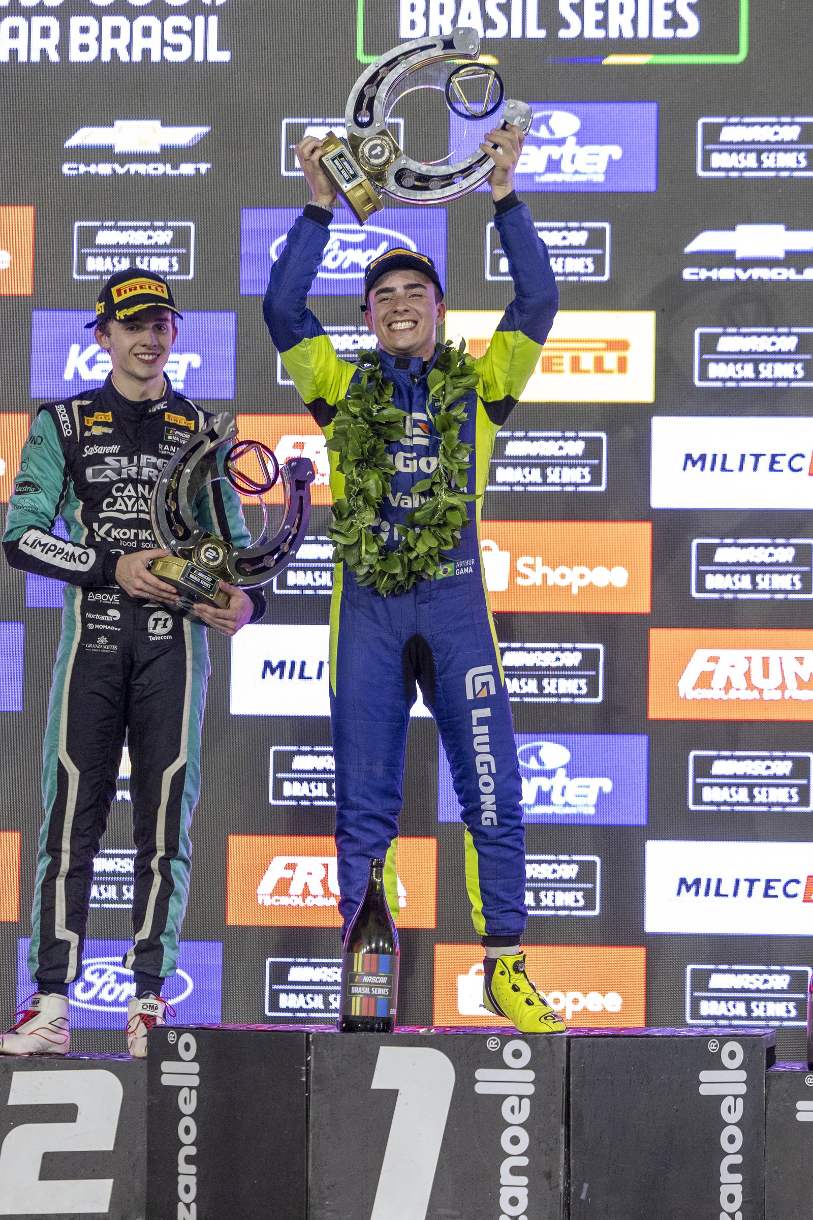 Arthur Gama ergue o troféu no alto do pódio após vencer a Night Challenge da NASCAR Brasil Series em Cuiabá, com Felipe Tozzo, segundo colocado, ao lado